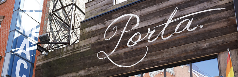 Wooden sign with white cursive writing that reads "Porta.", an eatery in Jersey City, New Jersey